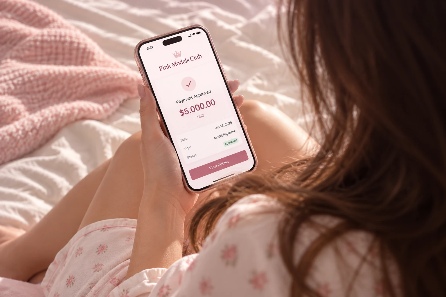 Modelo mirando su teléfono con una pantalla ilustrativa de pago aprobado de $5,000 de Pink Models Club